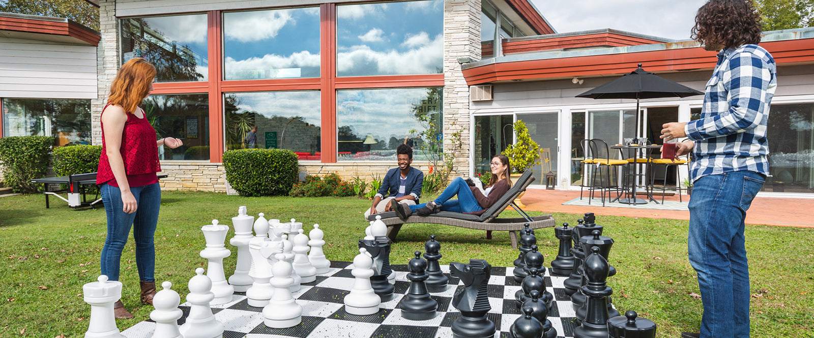Young couples playing chess with a giant chess set outside in a backyard.