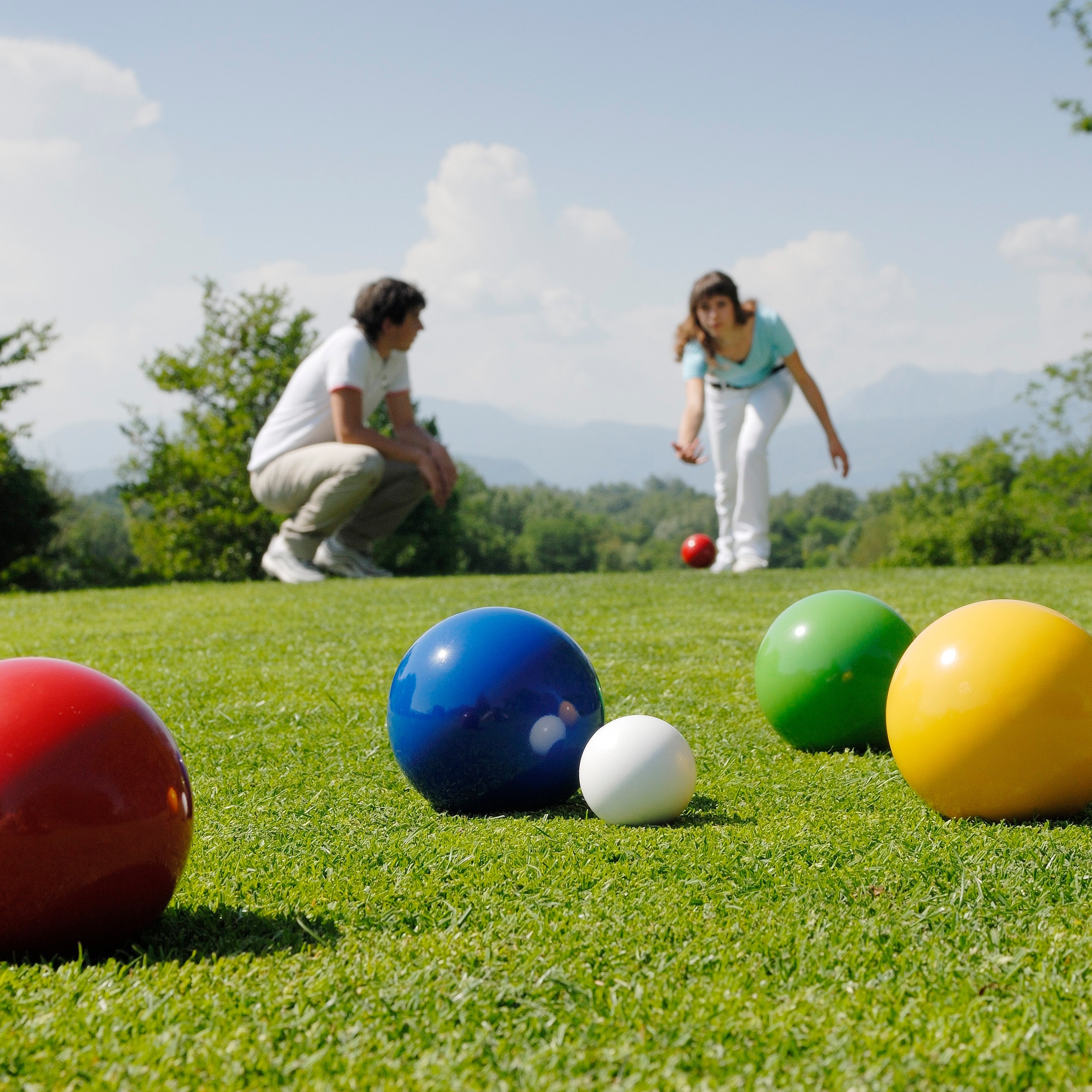 Couple playing bocce outside in an open lawn.
