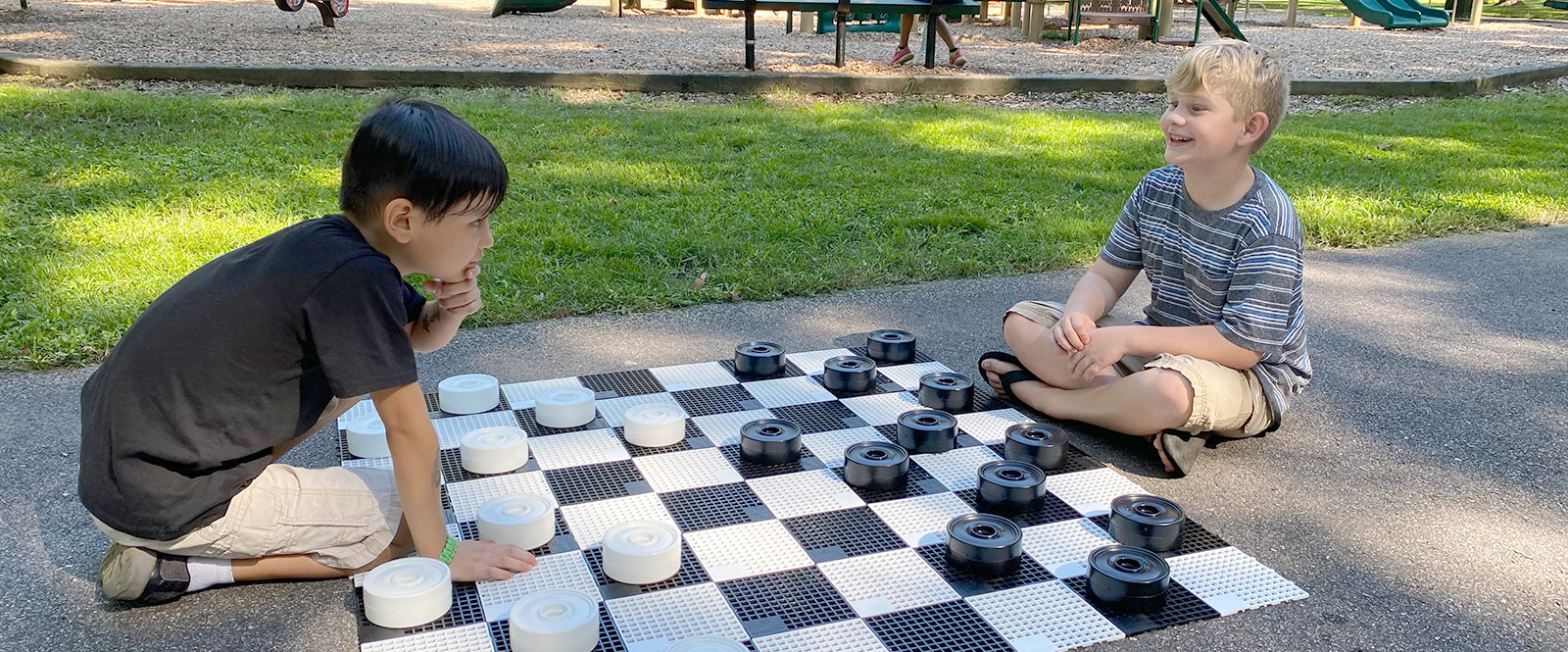 Two young boys play outdoor checkers in the park.