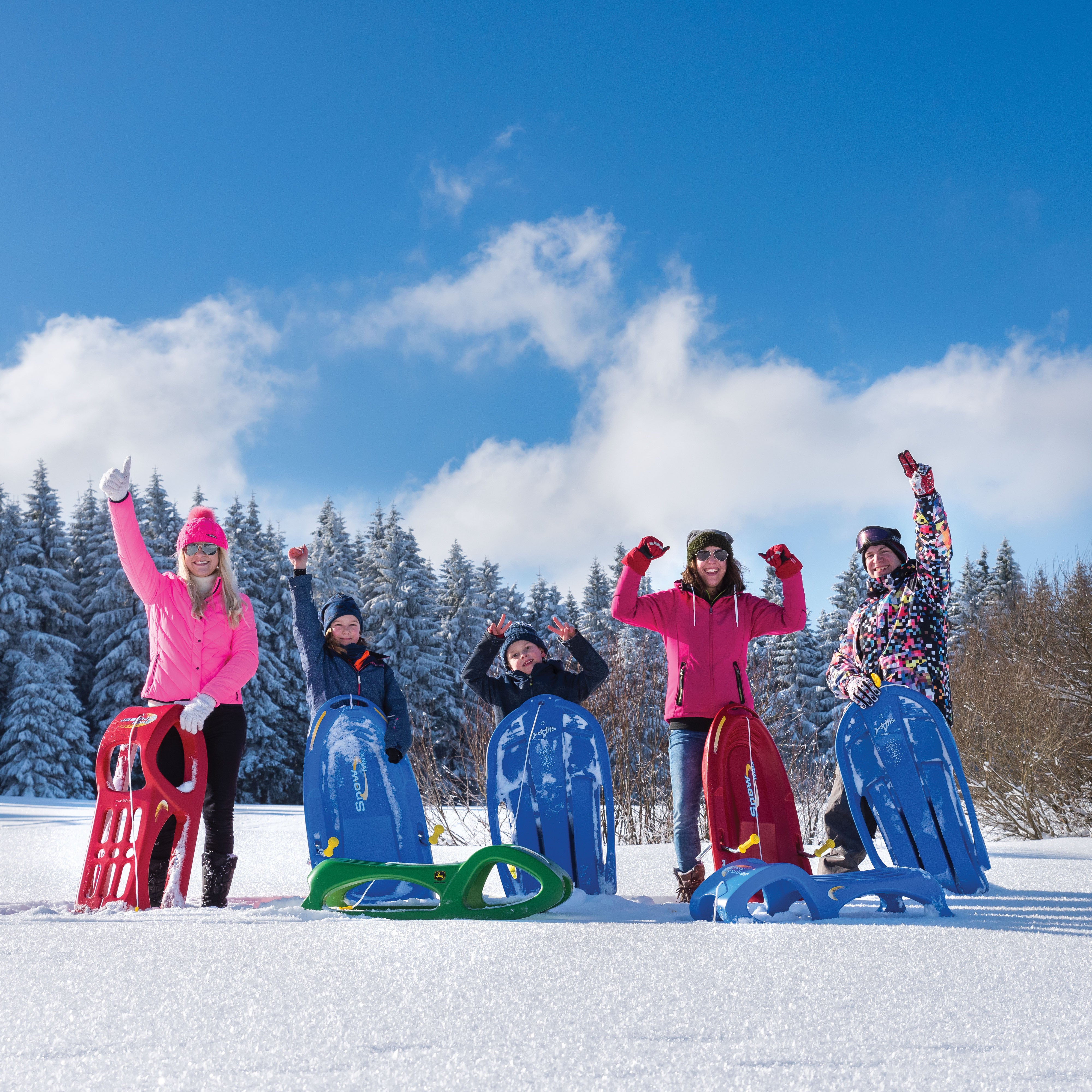Group of young people standing in the snow celebrating with their sleds.