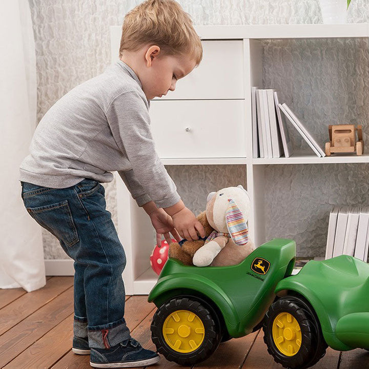 Lifestyle image of child using foot to floor resin tractor to transport stuffed animals 