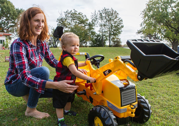 Child and parent operating digger on yellow pedal vehicle 