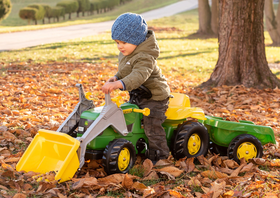 Lifestyle image of child using ride on tractor with functional front loader and trailer attachment 